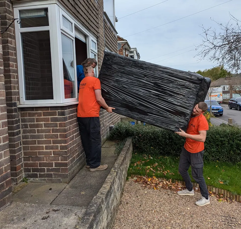 Two Ravenhill Removals team members carrying a protected sofa from a home Two Ravenhill Removals team members carrying a protected sofa from a home