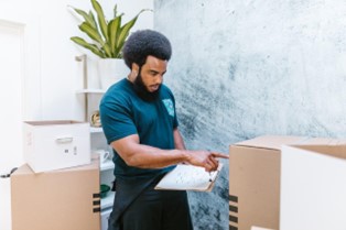 A man in a blue shirt with moving boxes and a checklist.